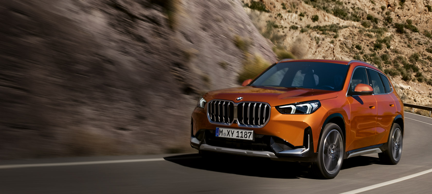 BMW X1 U11 xLine Utah Orange metalizado, vista de tres cuartos del frontal, en marcha en carretera